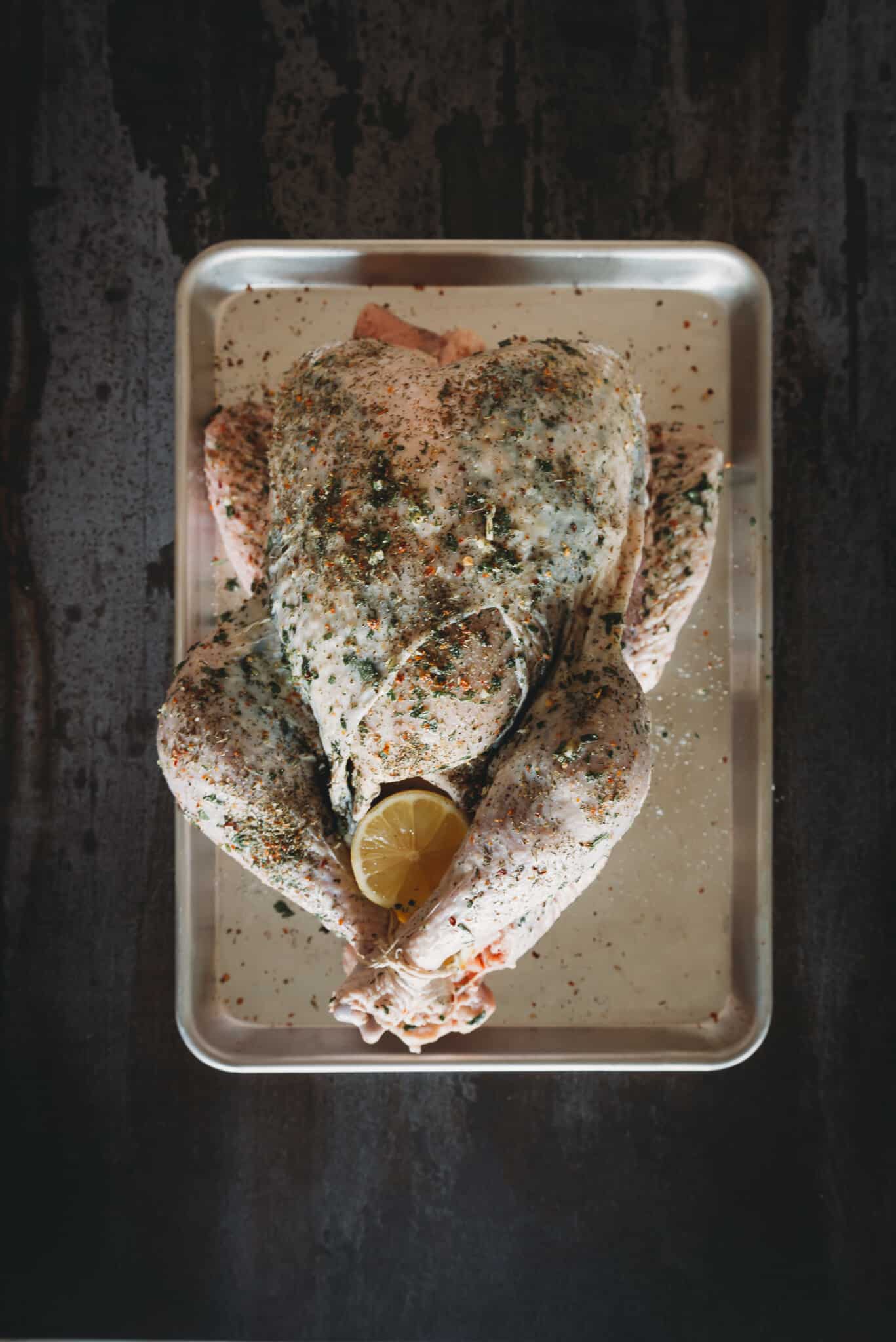 Above shot of raw turkey rubbed with herbs. 