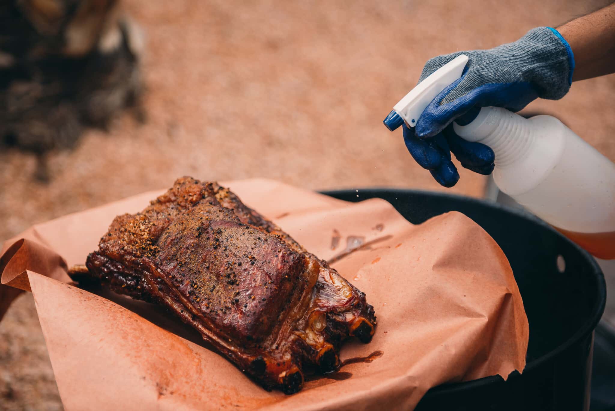 Beef ribs being spritzed with a mop while smokng. 