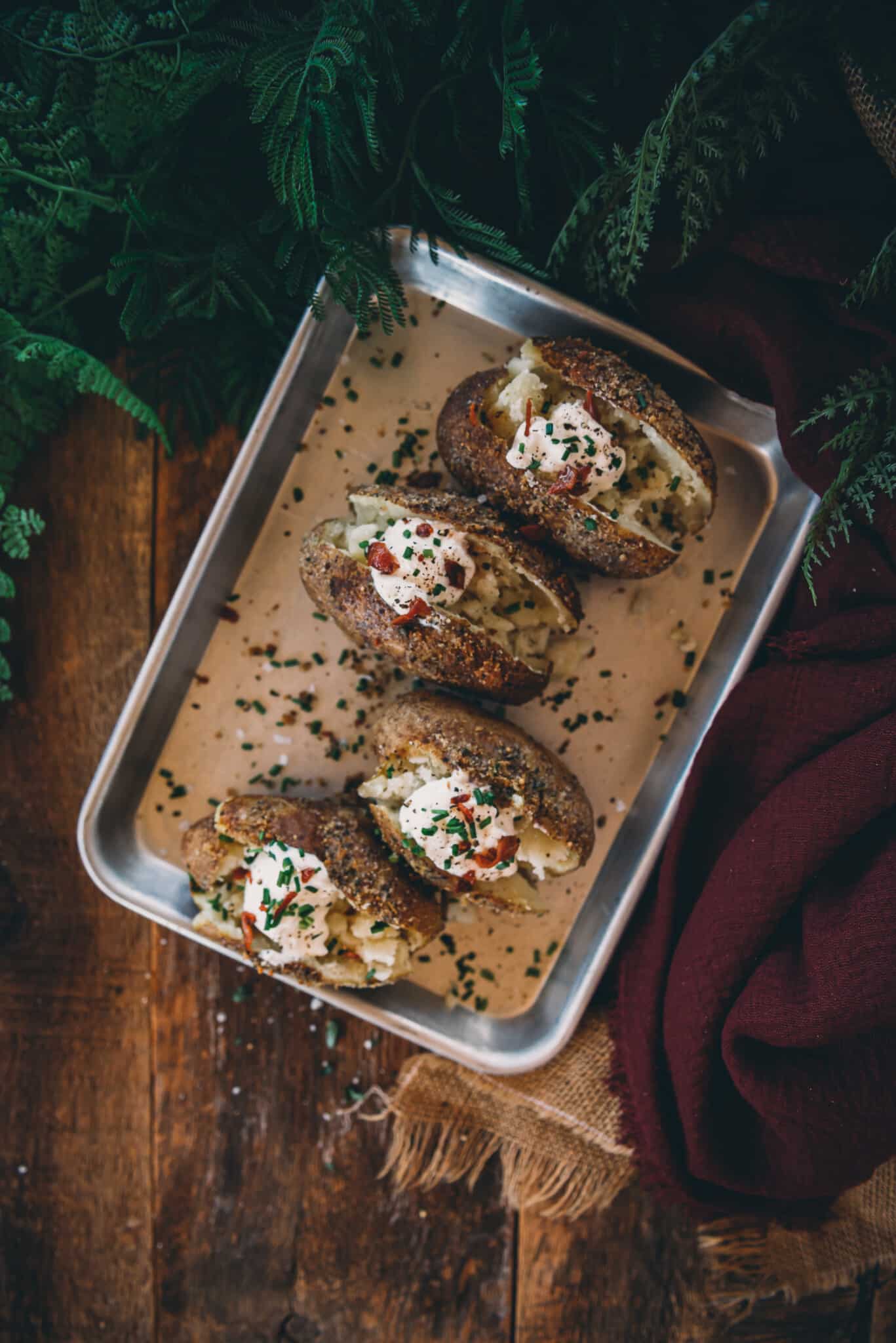 Overhead shot of smoked potatoes split to show fluffy flesh and topped with sour cream, chives and bacon all lined up on a serving tray. 