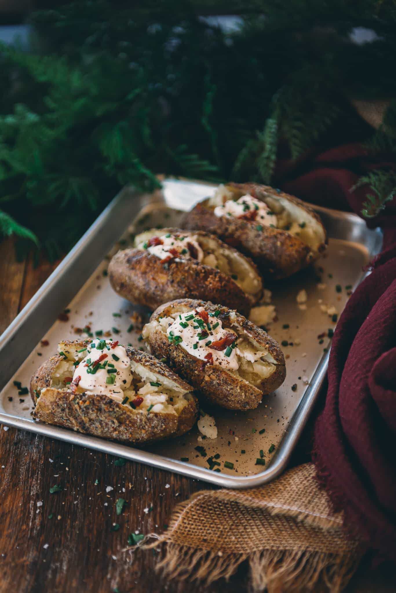Smoked baked potatoes lined up on a serving tray with toppings. 