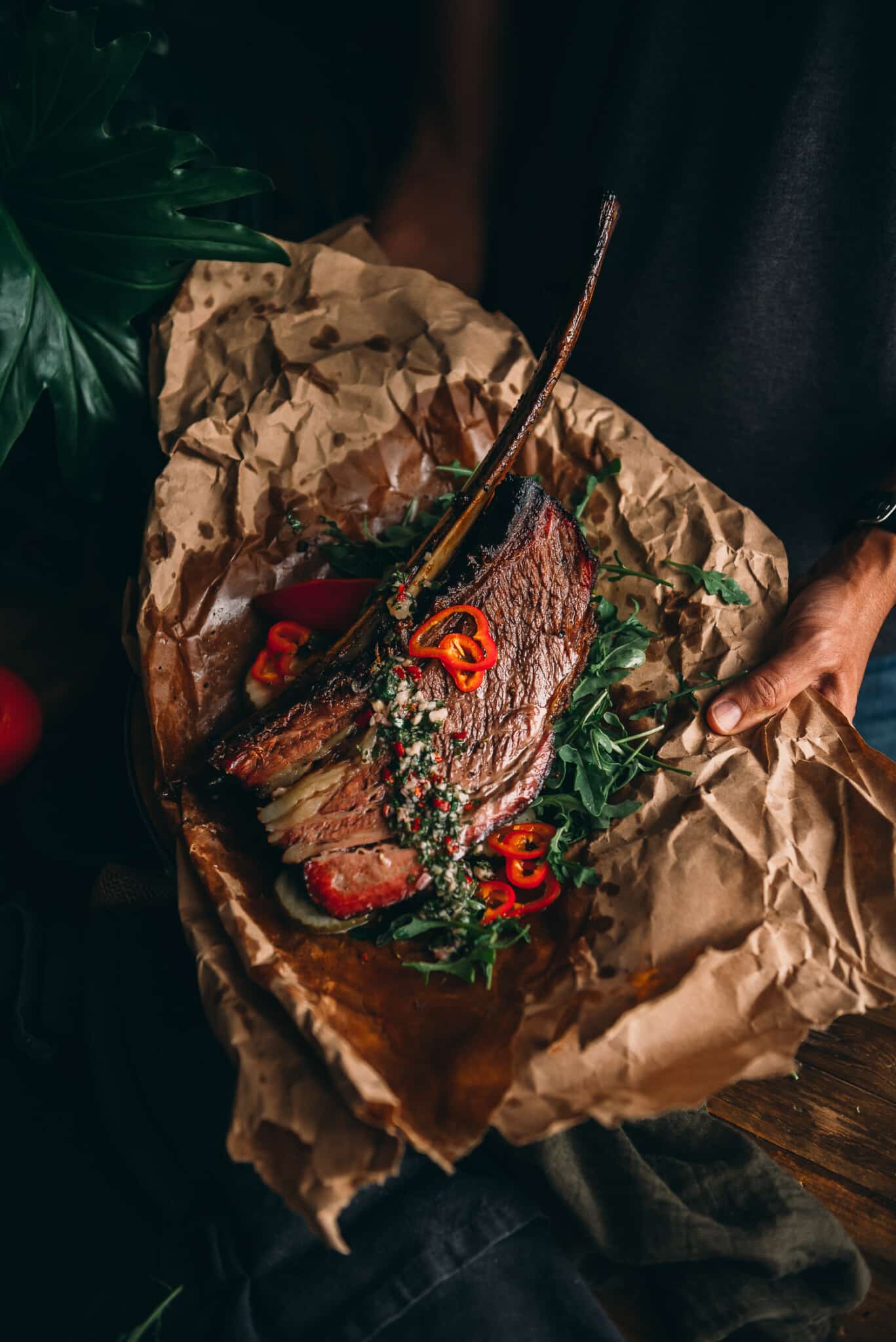 Hand presenting platter with giant beef rib on it. 