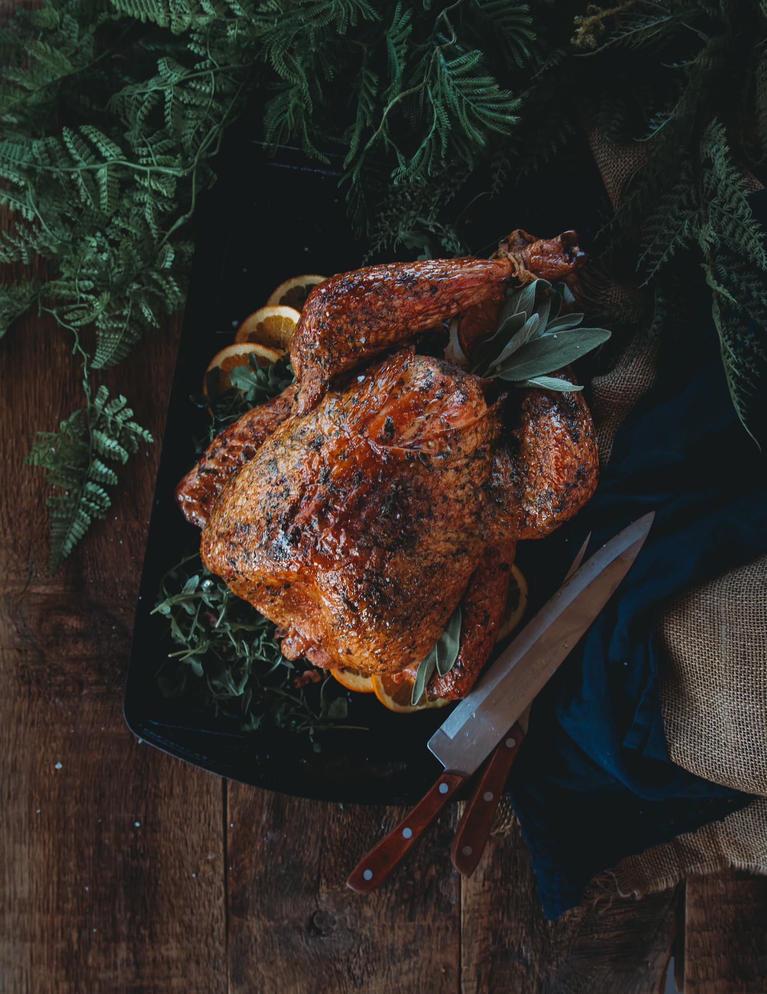 Above shot of smoked turkey with golden brown skin rubbed with herbs on a platter with carving knife nearby.