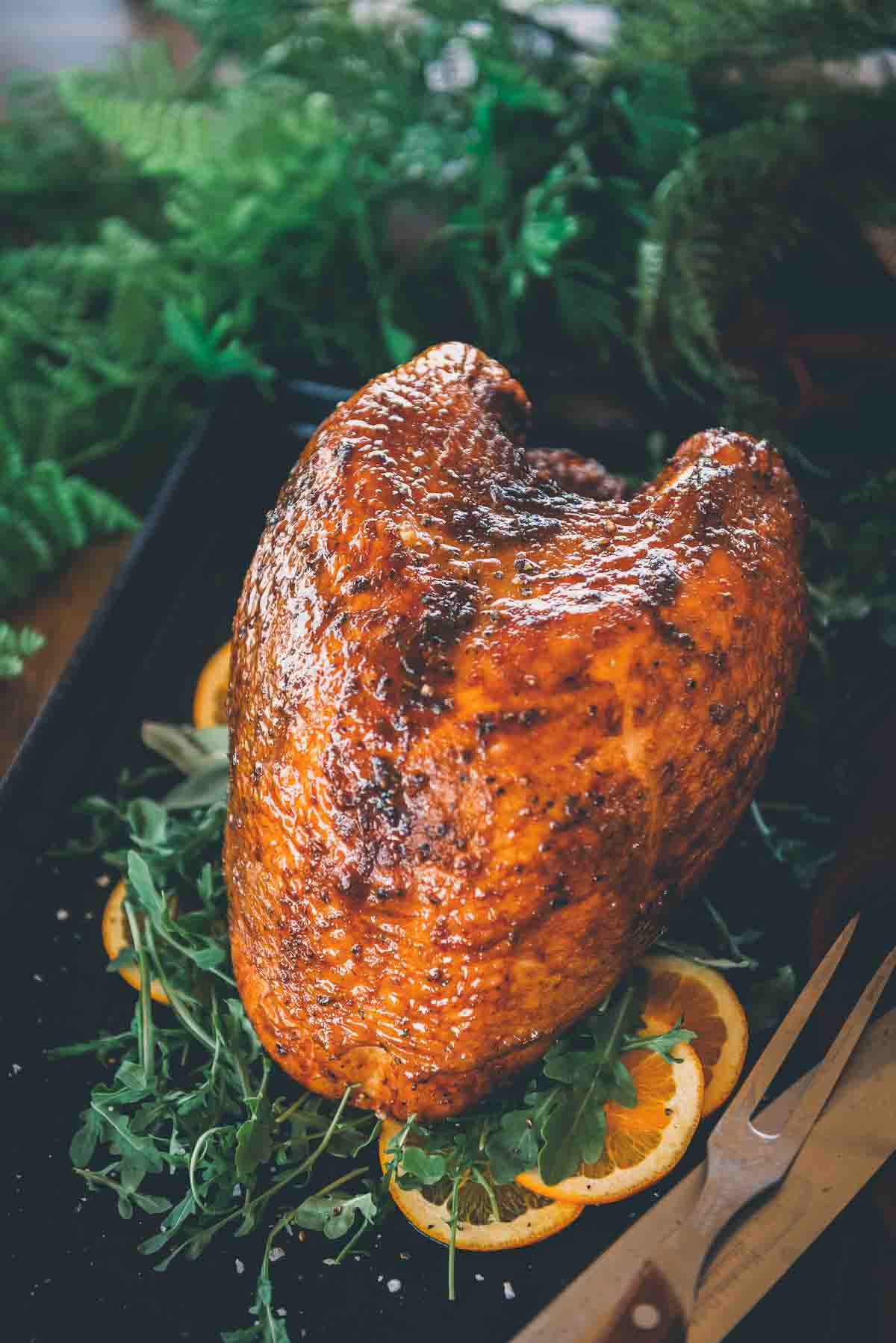 Close up of smoked turkey breast with crispy glazed skin over arugula and orange slices. 