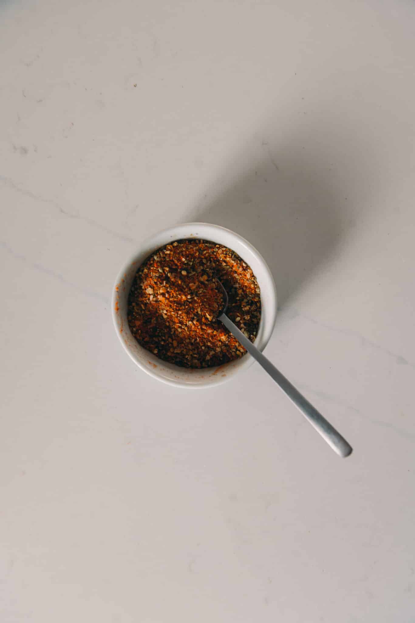 Red spices in a small white bowl on a white background. 