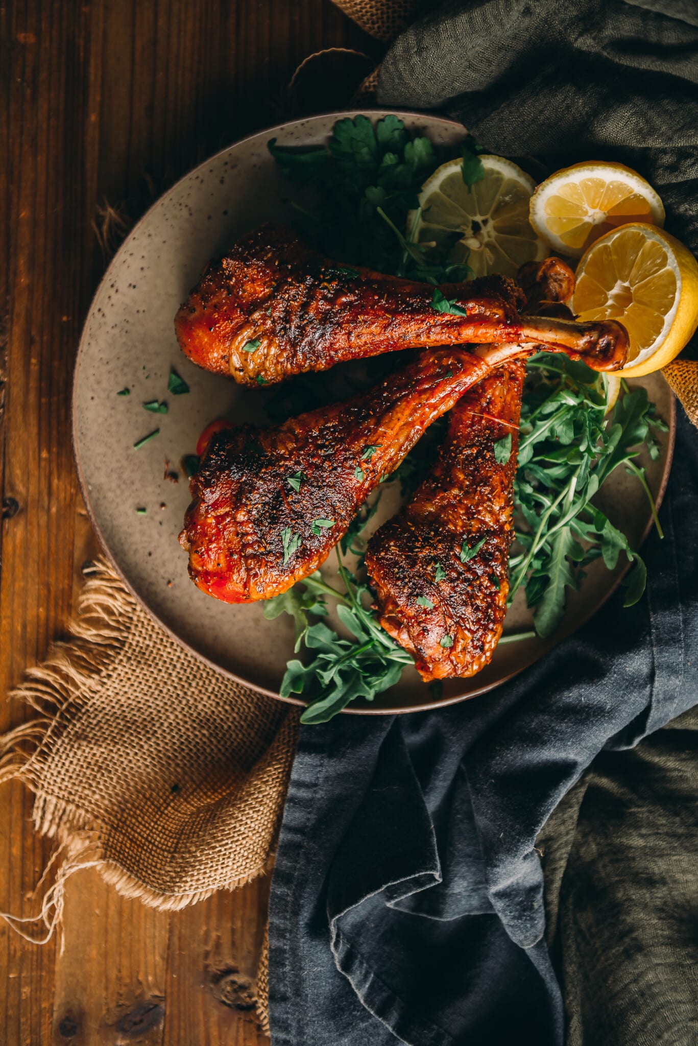 3 smoked turkey legs of an amber color on a platter over arugula and sliced lemon. 