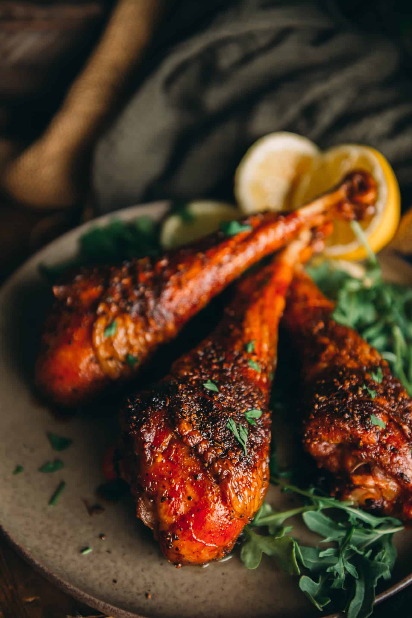 Close up of smoked turkey legs on platter, showing crispy red skin and juicy dark meat garnished with parsley. 