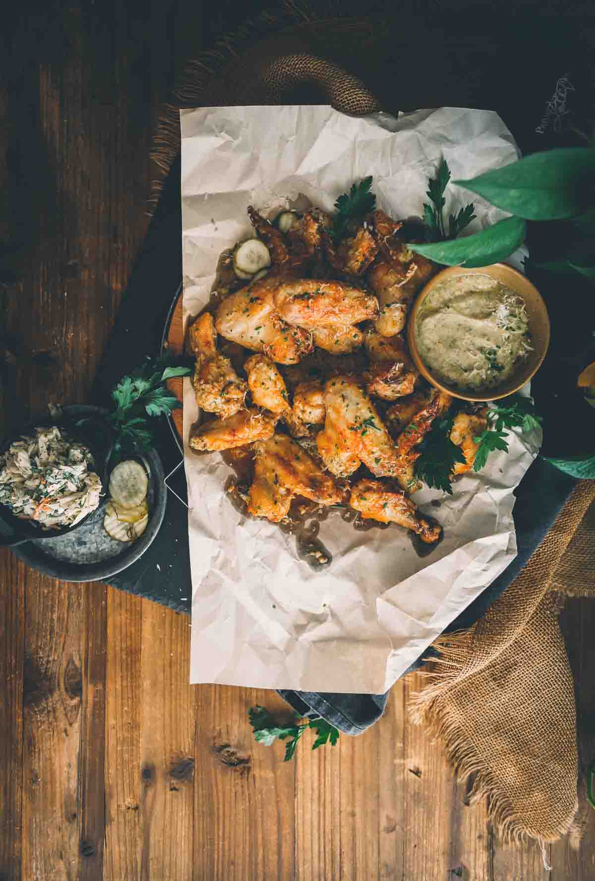 Overhead shot of crispy golden chicken wings on a platter with dipping sauce, pickles, and slaw. 