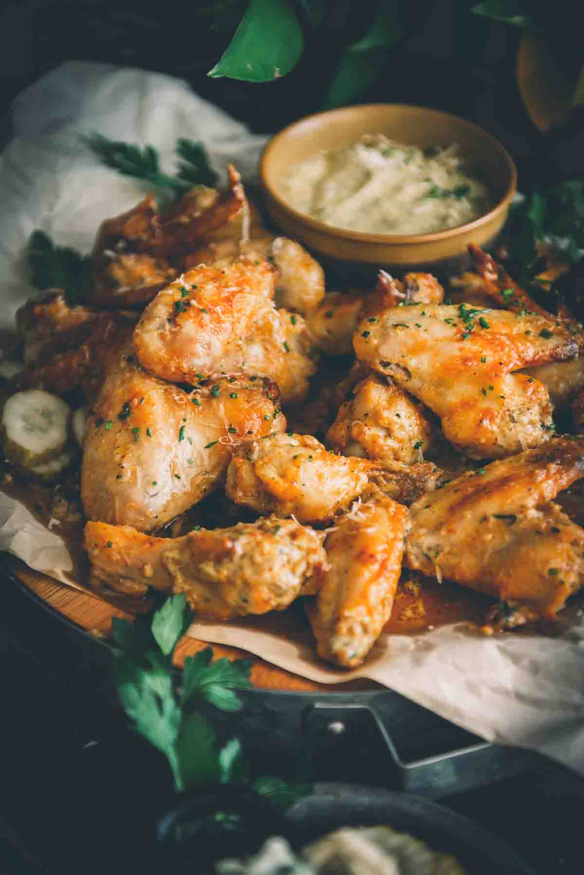 Close up platter of air fried chicken wings garnished in chives and grated cheese. 