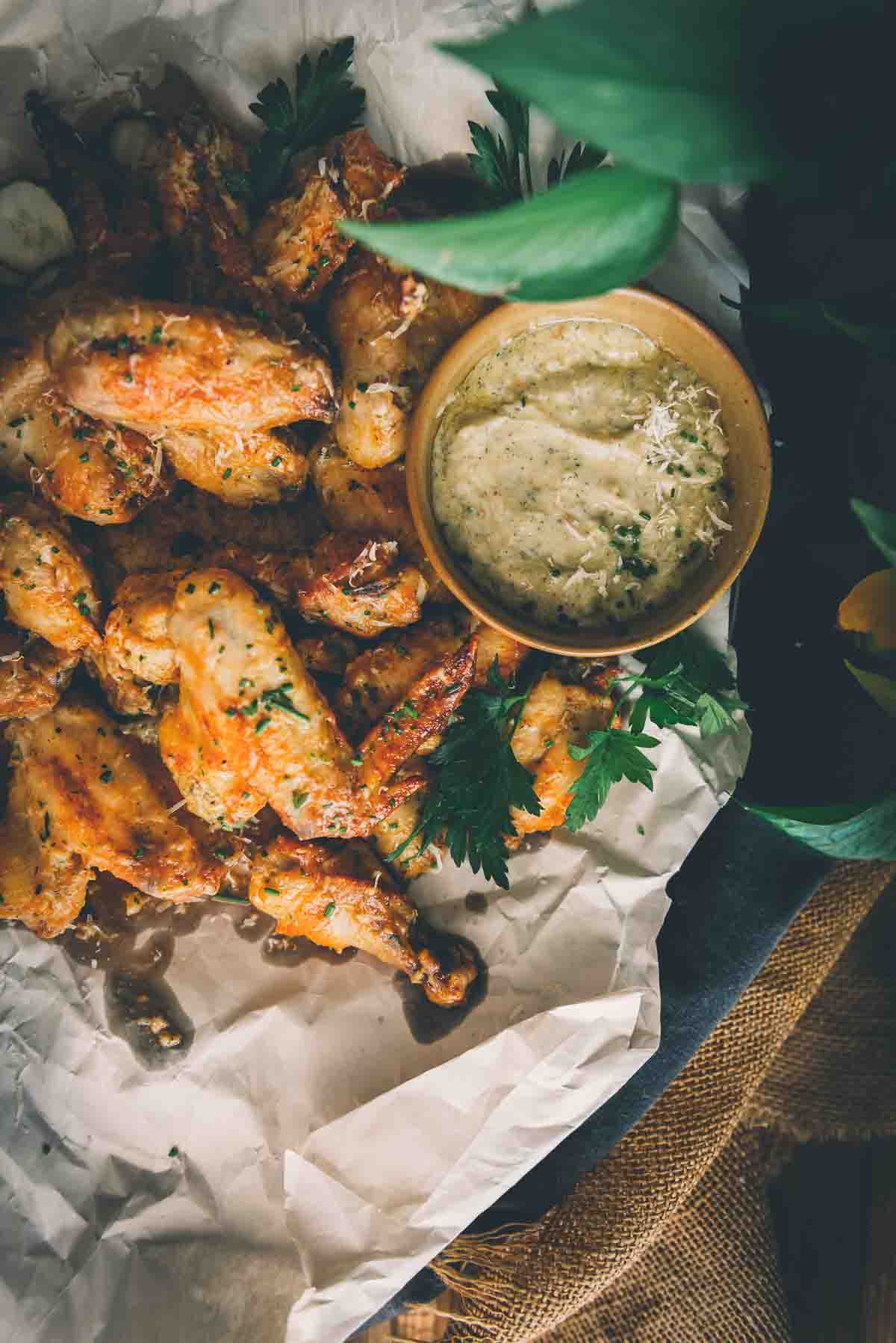 Overhead shot of platter of chicken wings with a garlic parm sauce in a bowl on the side. 