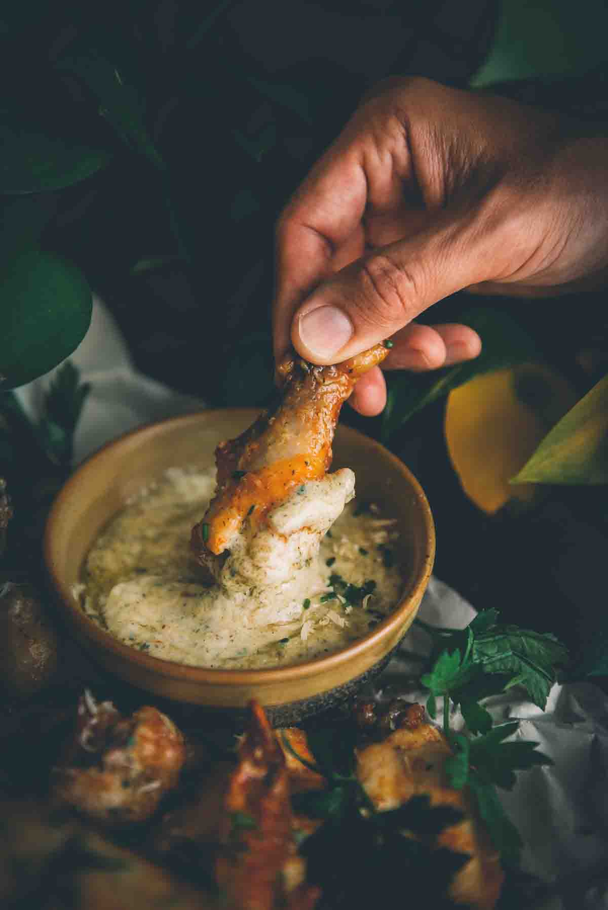 Close up of hand dipping wing into garlic parmesan wing sauce.