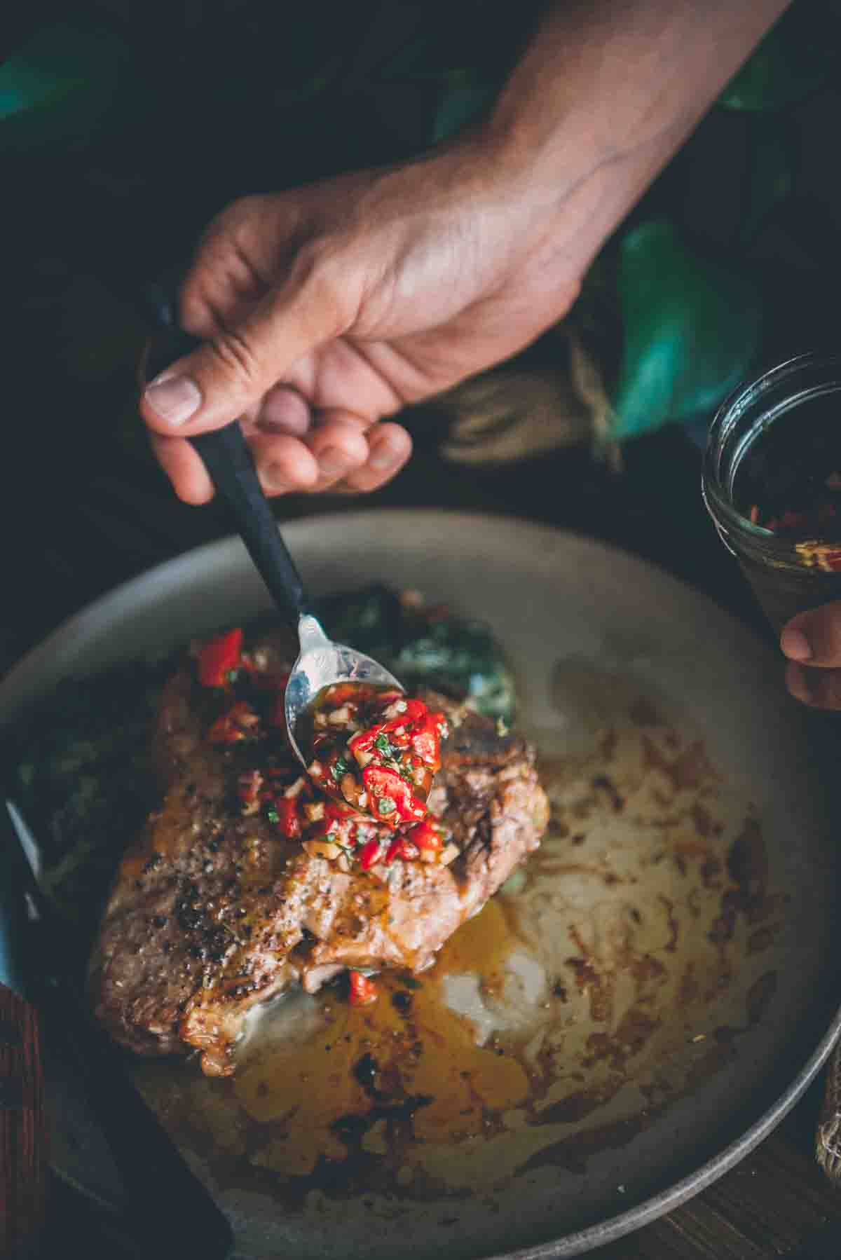 Hand spooning rojo chimichurri over meat. 