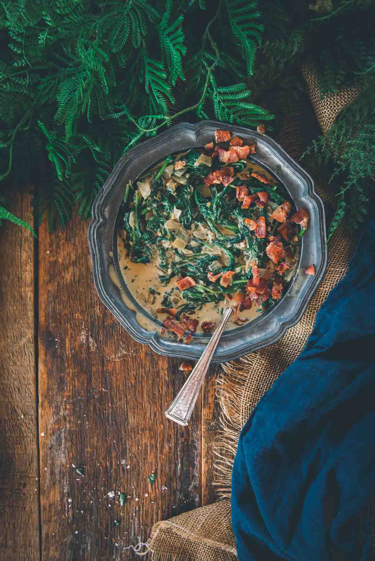 Overhead shot of low carb creamed spinach with bacon in a pewter bowl with a spoon on a wooden background.