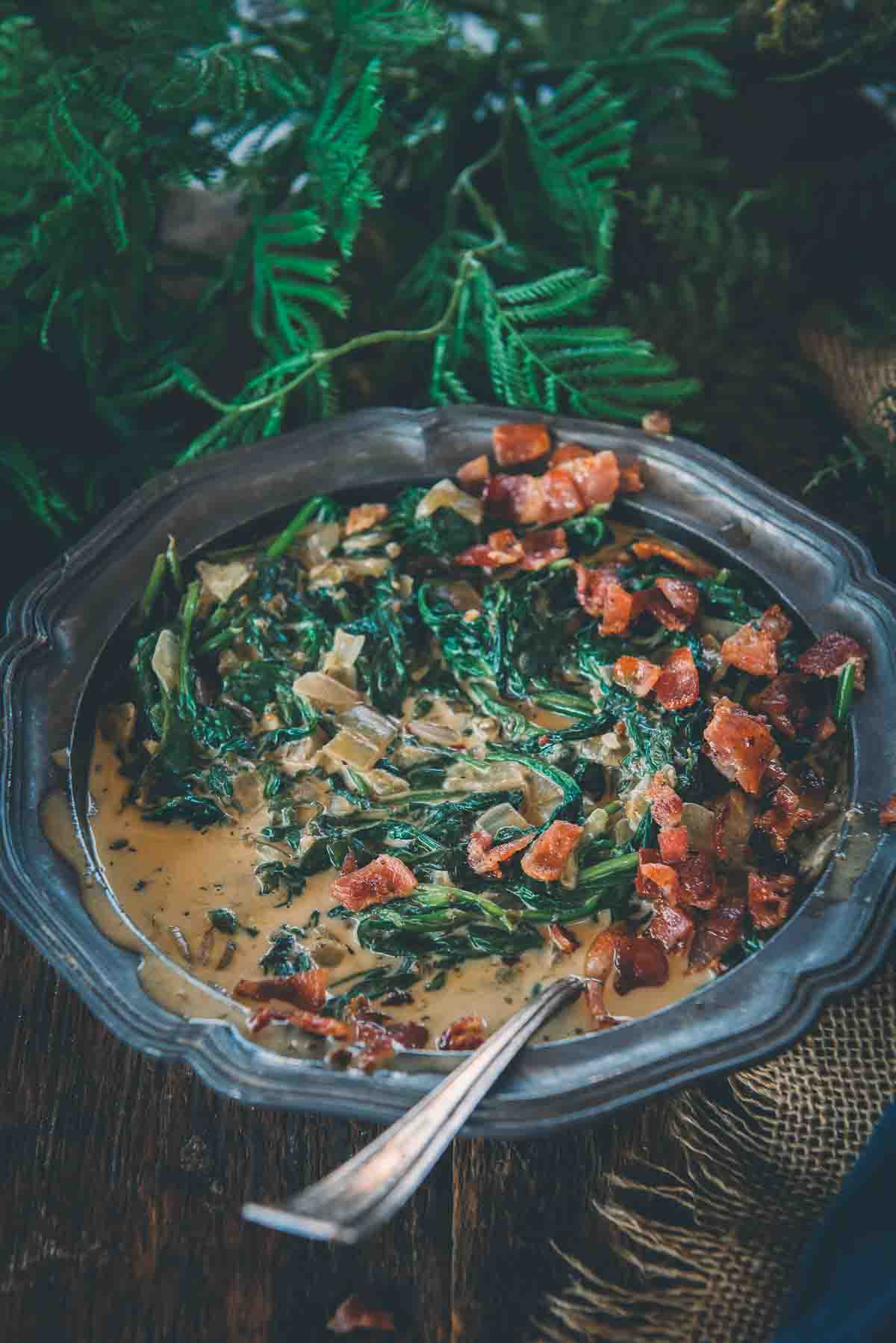 Creamed spinach in a metal bowl with bacon on top. 