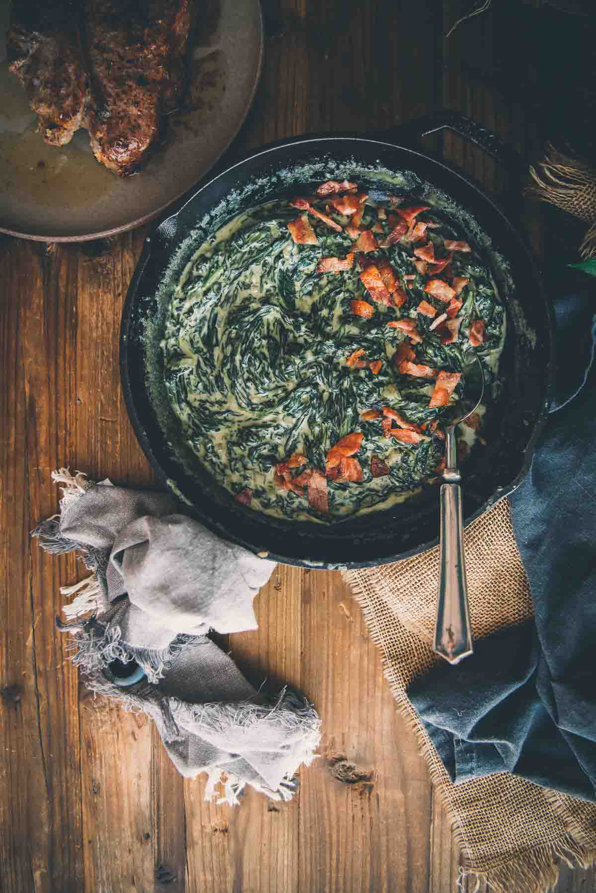 Overhead shot of creamed spinach in a cast iron skillet on a wooden table.