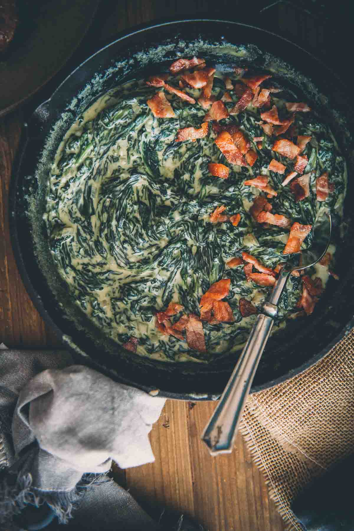 Close up of keto creamed spinach in a cast iron skillet topped with crumbled bacon.