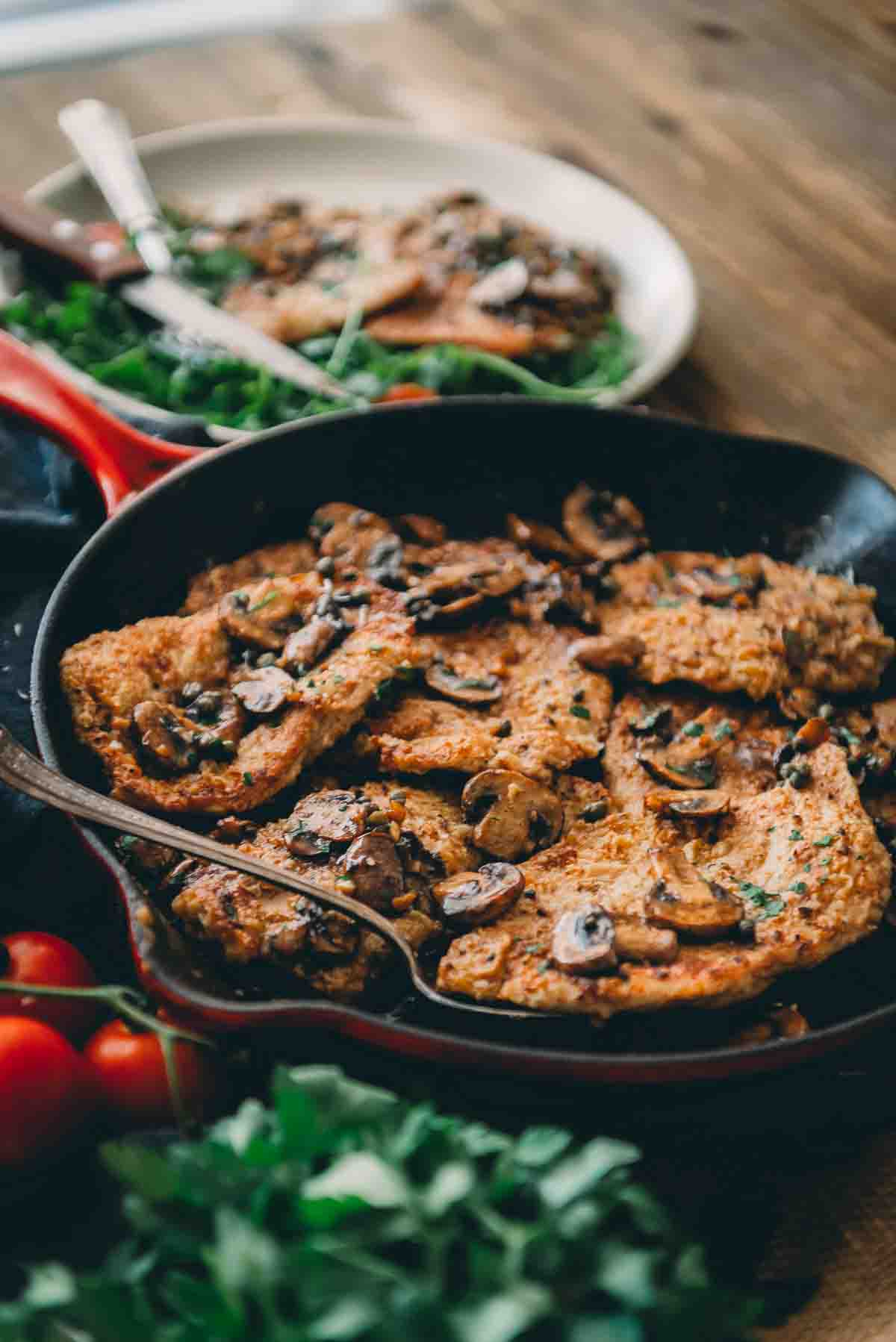 Backlit shot of veal scallopini in a skillet with mushrooms on top.  