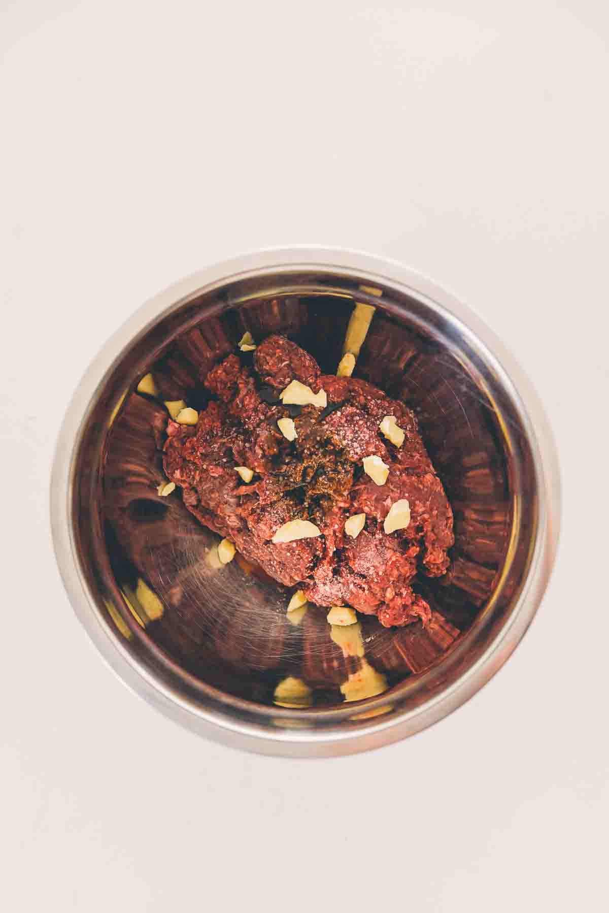 Raw venison meat in a bowl with seasonings and butter.