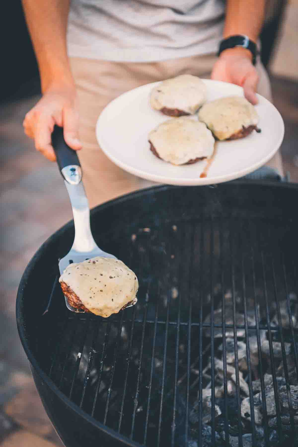 Hand using spatula to lift burgers from grill grates. 
