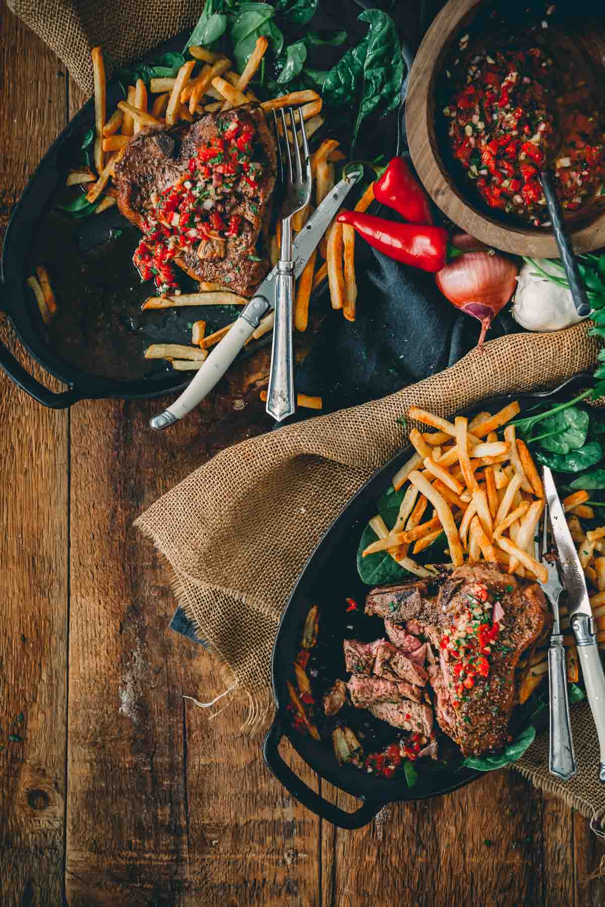 Showing a meal of pan seared veal chops on plates on a rustic wooden background. 