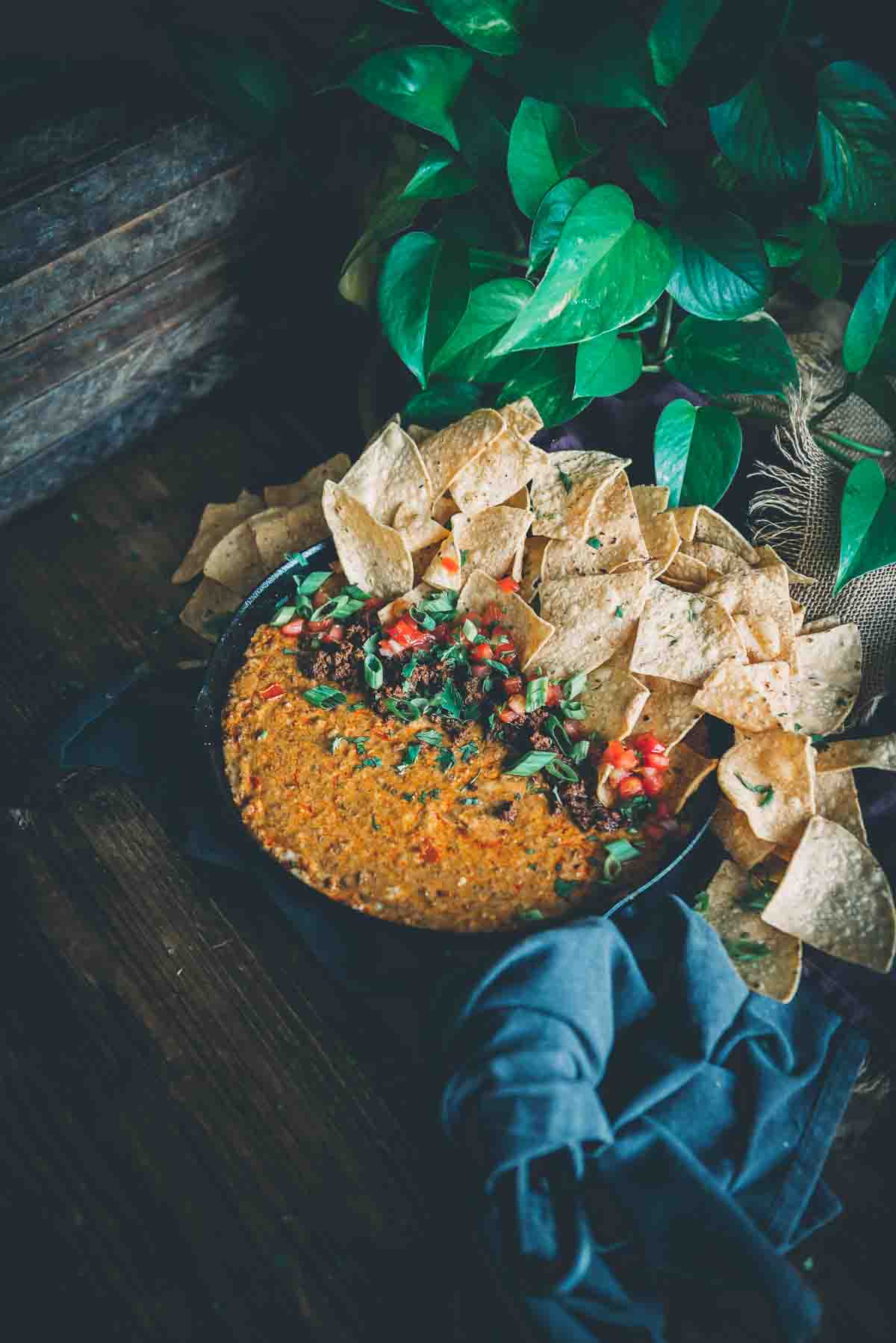 Cast iron skillet filled with melted smoked cheese dip topped with colorful garnish of pico de gallo,  minced scallions, and tortilla chips.