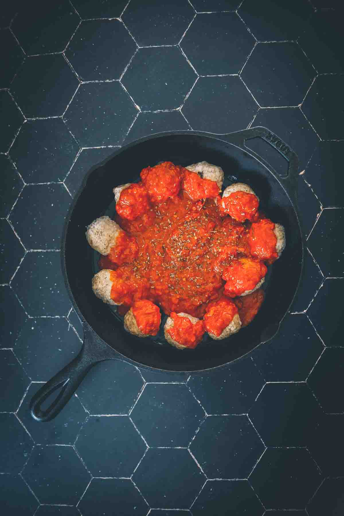 Frozen meatballs in a skillet covered in red sauce and spices. 