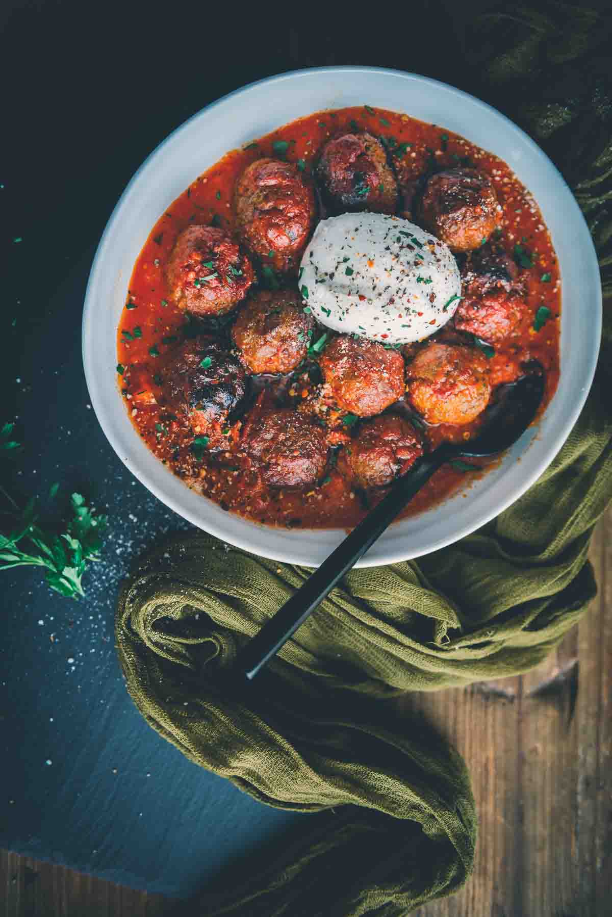 Cooked meatballs rolled in red sauce with burrata in the center sprinkled with herbs. 