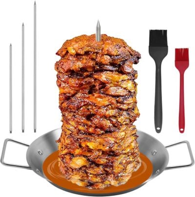 A vertical stack of grilled meat on a skewer sits in a pan, surrounded by four skewers and two basting brushes. Perfect for those who appreciate the art of cooking, this setup could be the ultimate grilling gift for enthusiasts.