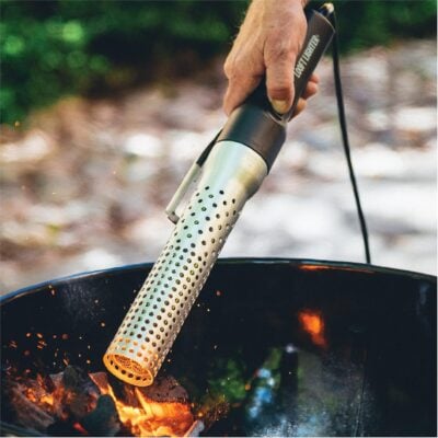 A person ignites charcoal with an electric fire starter in a barbecue grill outdoors, showcasing one of the finest grilling gifts for any BBQ enthusiast.