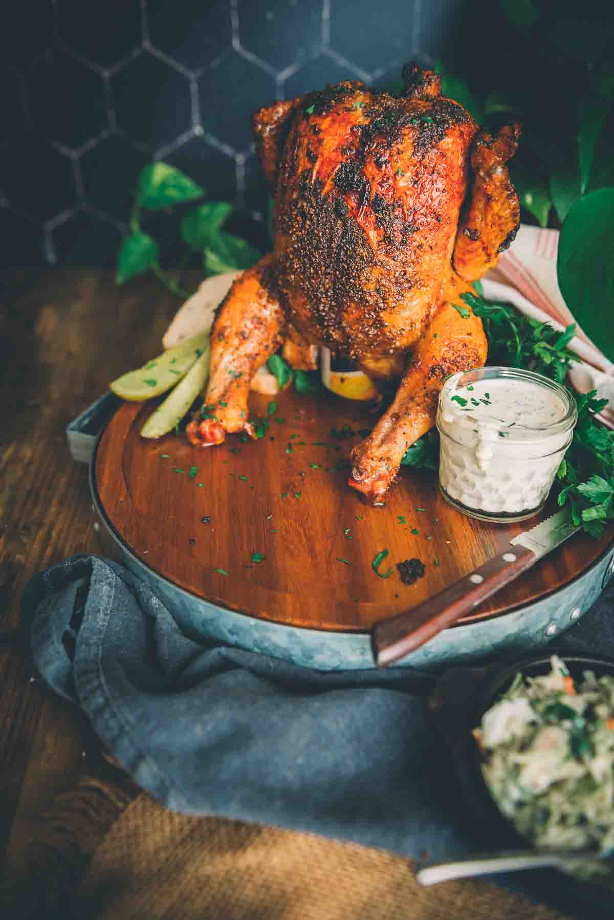 Cooked chicken nestled atop a beer can on a serving platter with alabama white sauce. 