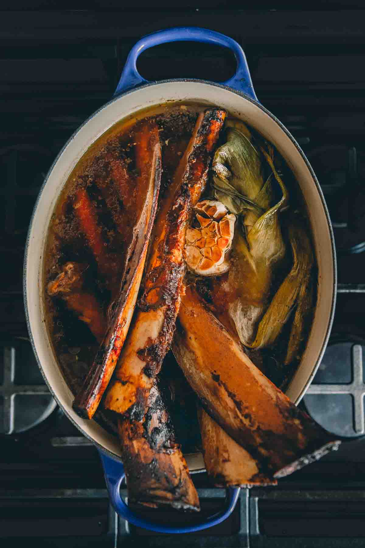 Dutch oven with roasted beef b ones and veggies in water.