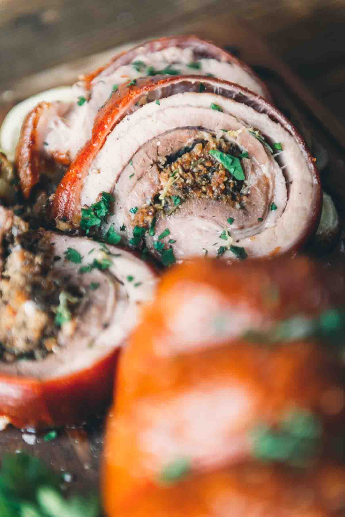 Close up of sliced porketta showing cooked rolled pork belly stuffed with filling and garnished with minched parsley and lemon zest. 