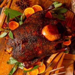 Roasted duck with oranges and sage on a wooden cutting board.