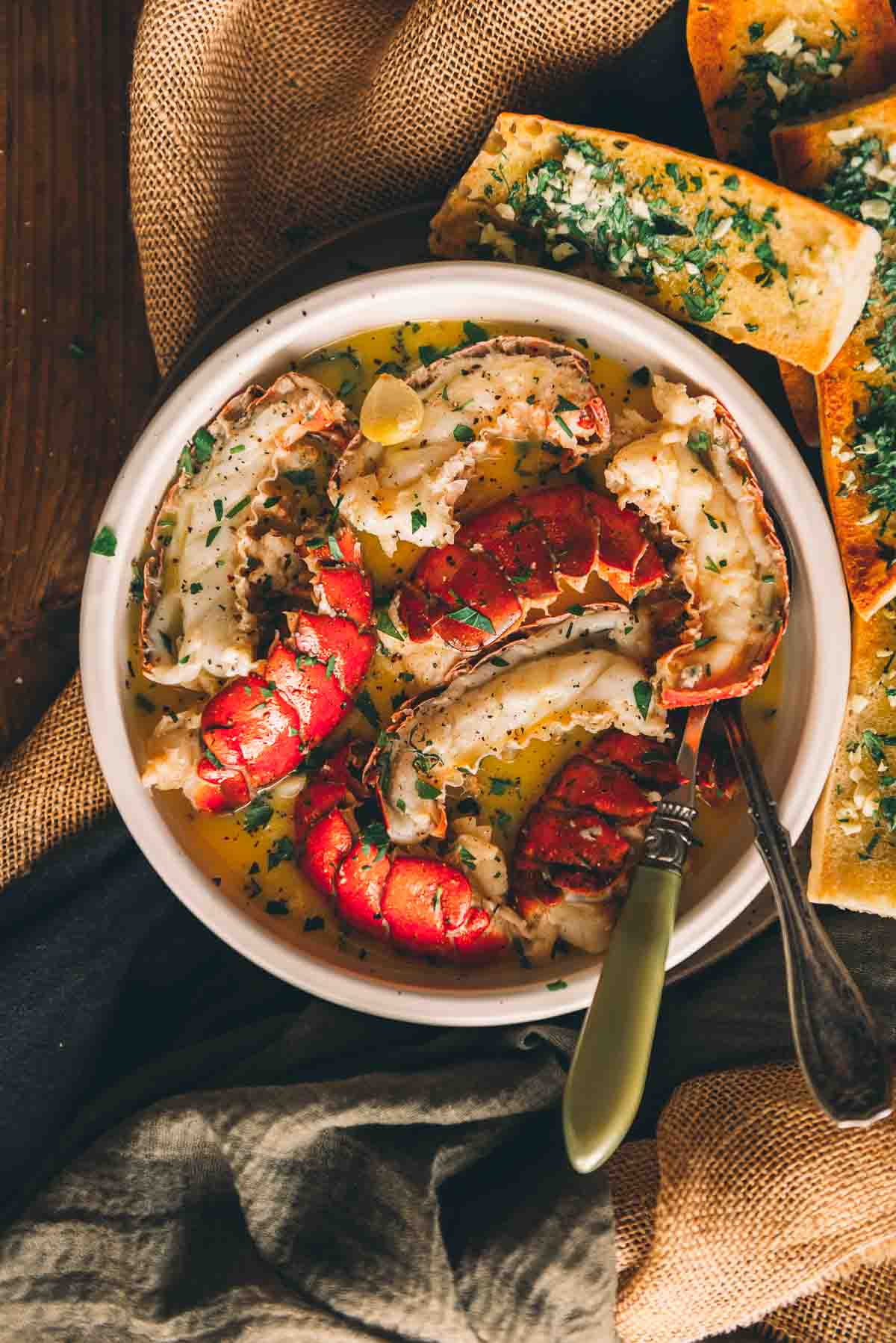 Bright red lobster shells and cooked lobster meat in a bowl of butter, garlic and herbs.