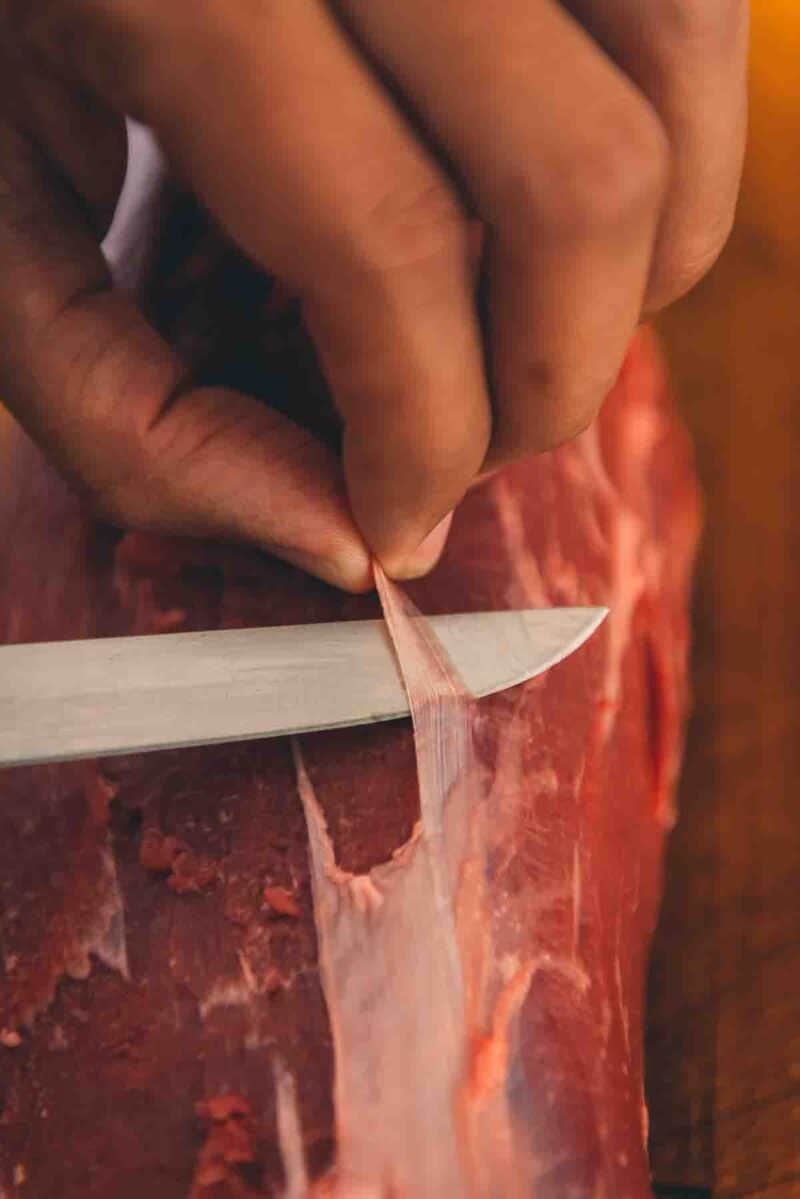 Demonstrating how to trim a beef tenderloin with a knife.