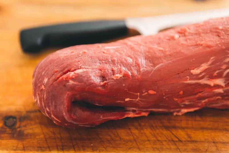 A piece of beef tenderloin on a cutting board with a knife.