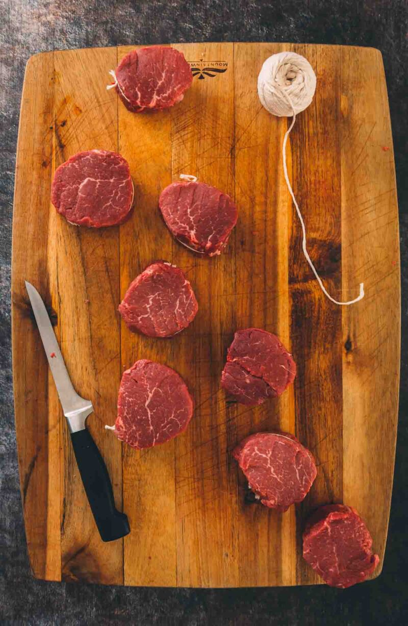 Beef steaks on a cutting board with a knife, demonstrating how to trim a beef tenderloin.