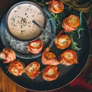 Bacon-wrapped scallops with a dip on a plate.