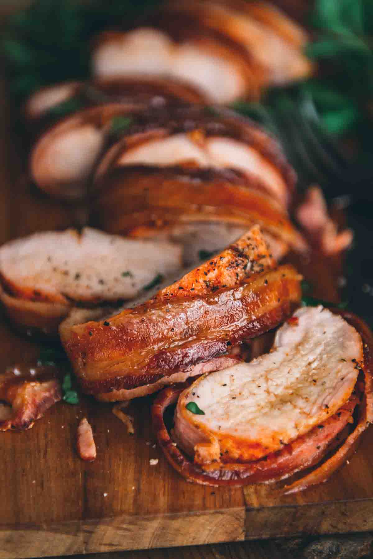 Close up shot of slice of bacon wrapped pork loin showing detail on spices and juicy meat. 