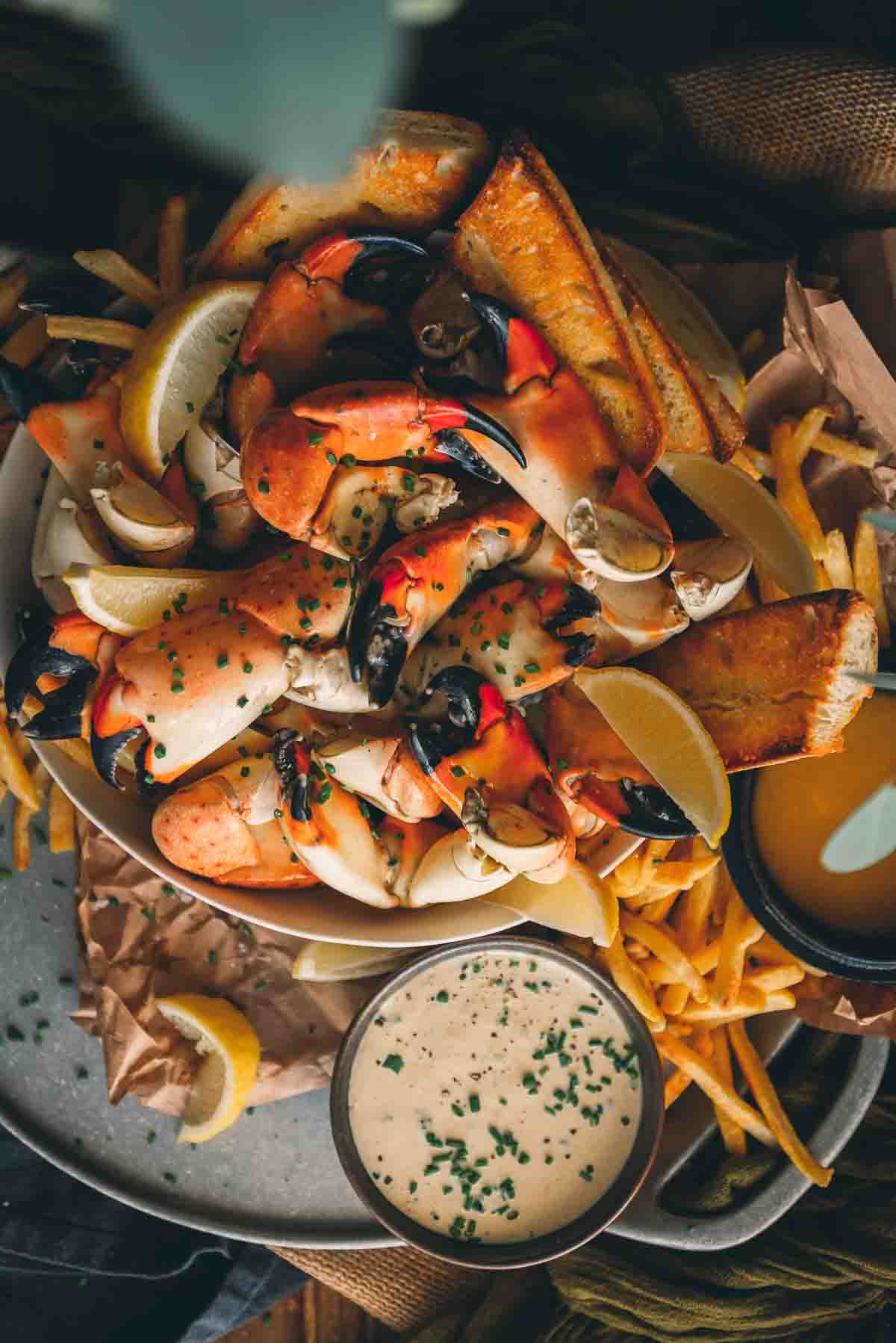Overhead shot o bowl overflowing with crab claws, lemon wedges, and toasted bread. 