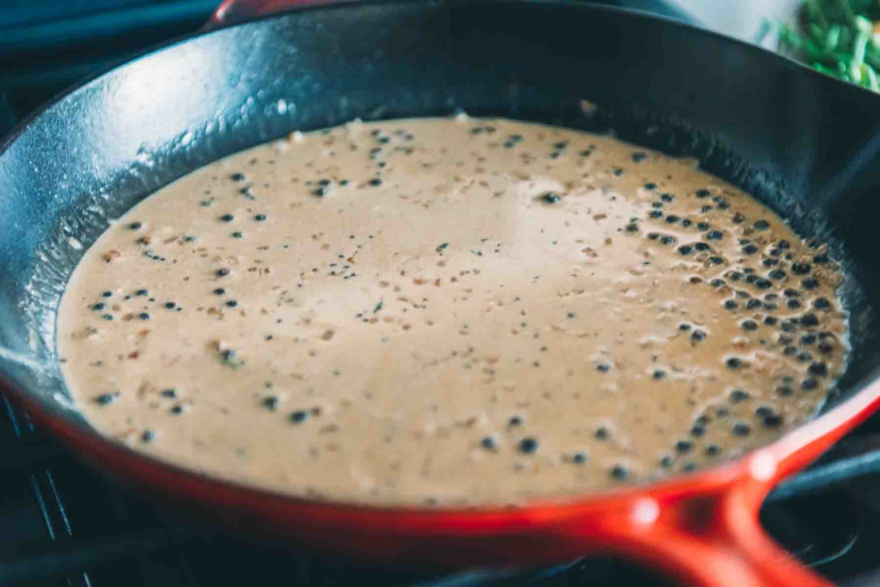 Cream added to peppercorn sauce in pan. 