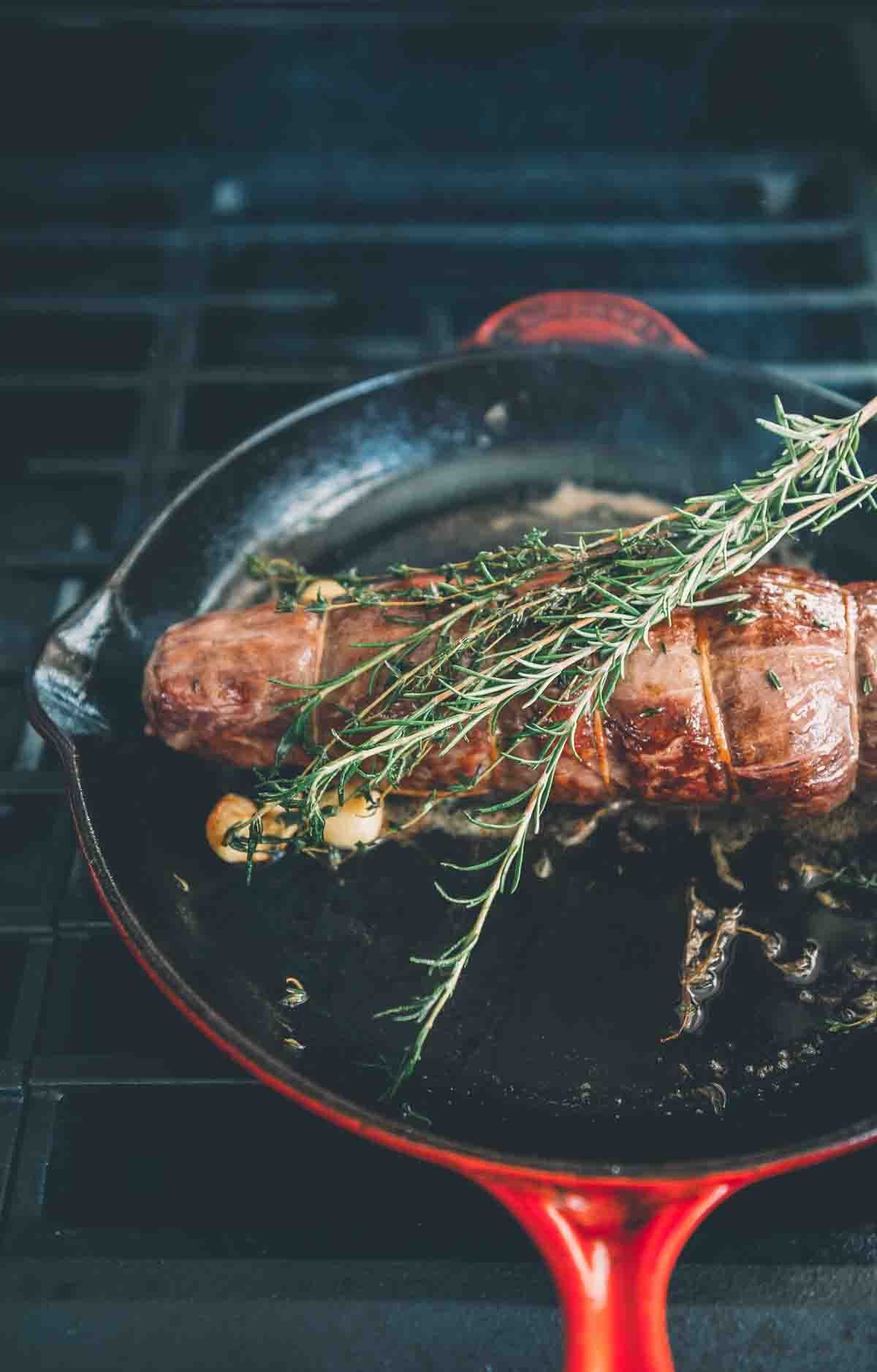 Sous vide beef tenderloin with a sprig of rosemary being seared in a pan.