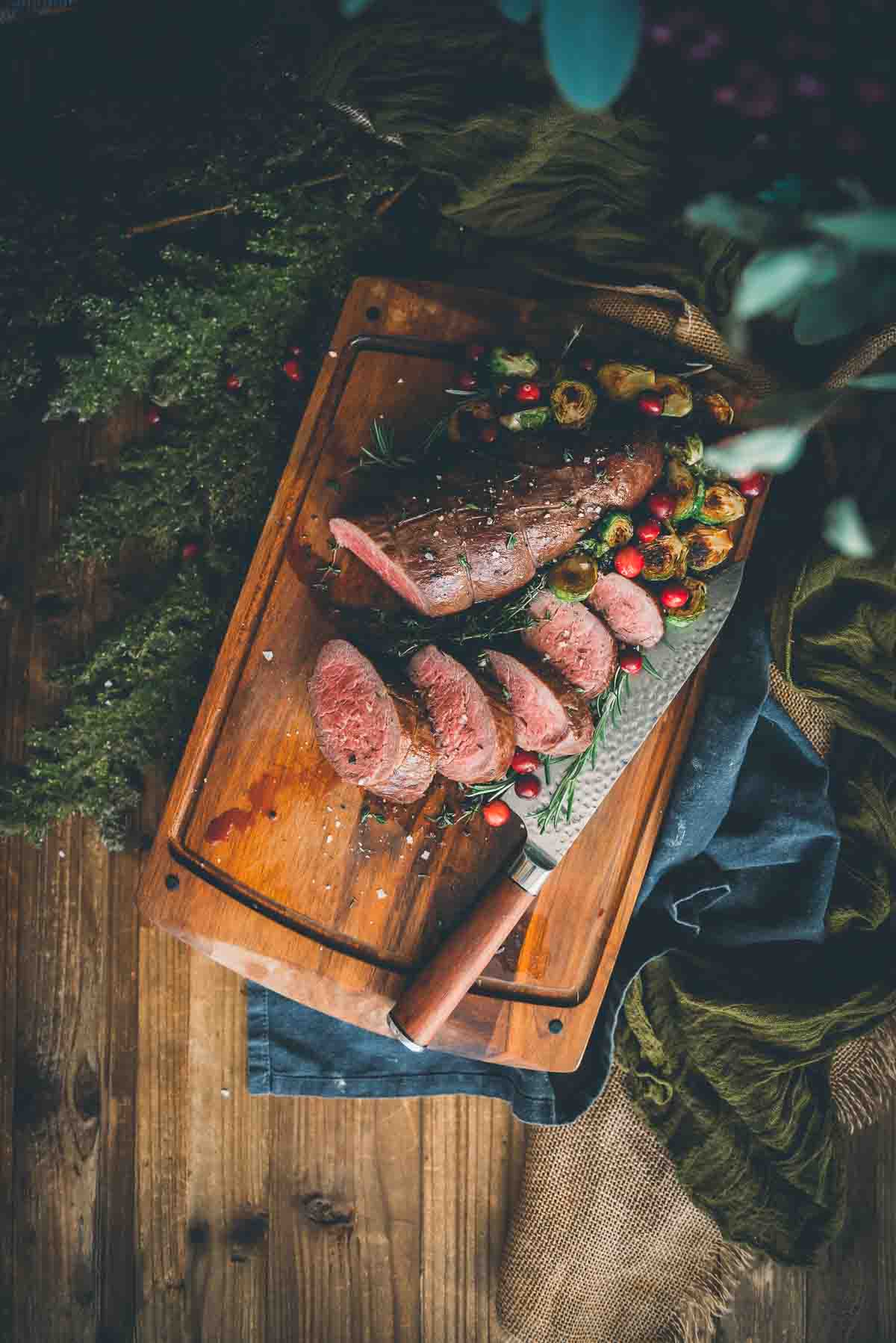 Overhead shot of a cooked beef roast on a serving board with veggies. 