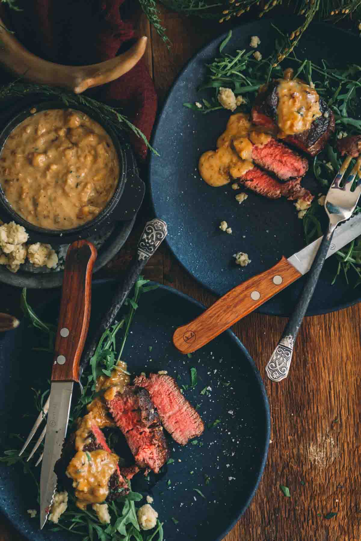 Overhead of plates with steaks showing medium rare centers and steak sauce spooned over top. 