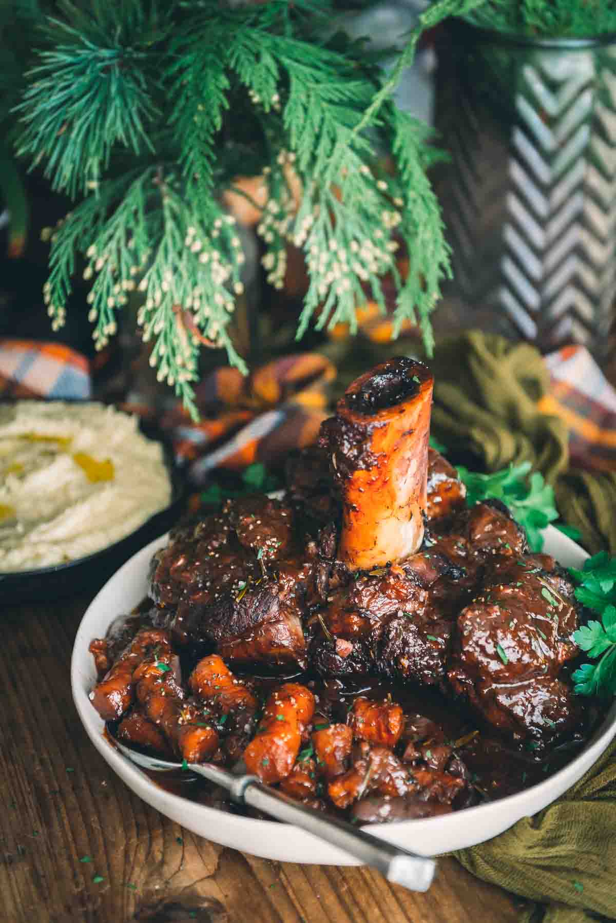 Braised beef shank with exposed bone, aka Thor's Hammer, set in a serving bowl with veggies. 