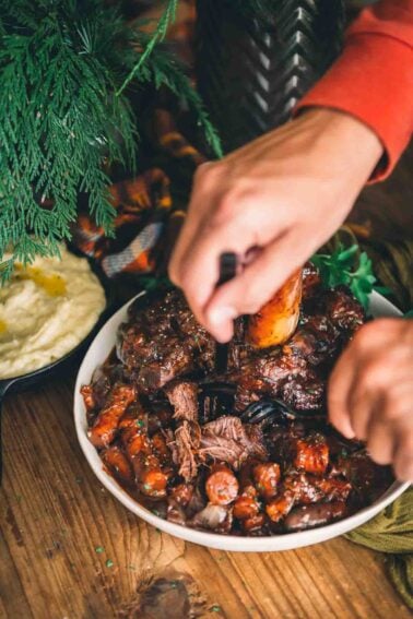 A person cutting braised beef shank on a plate.