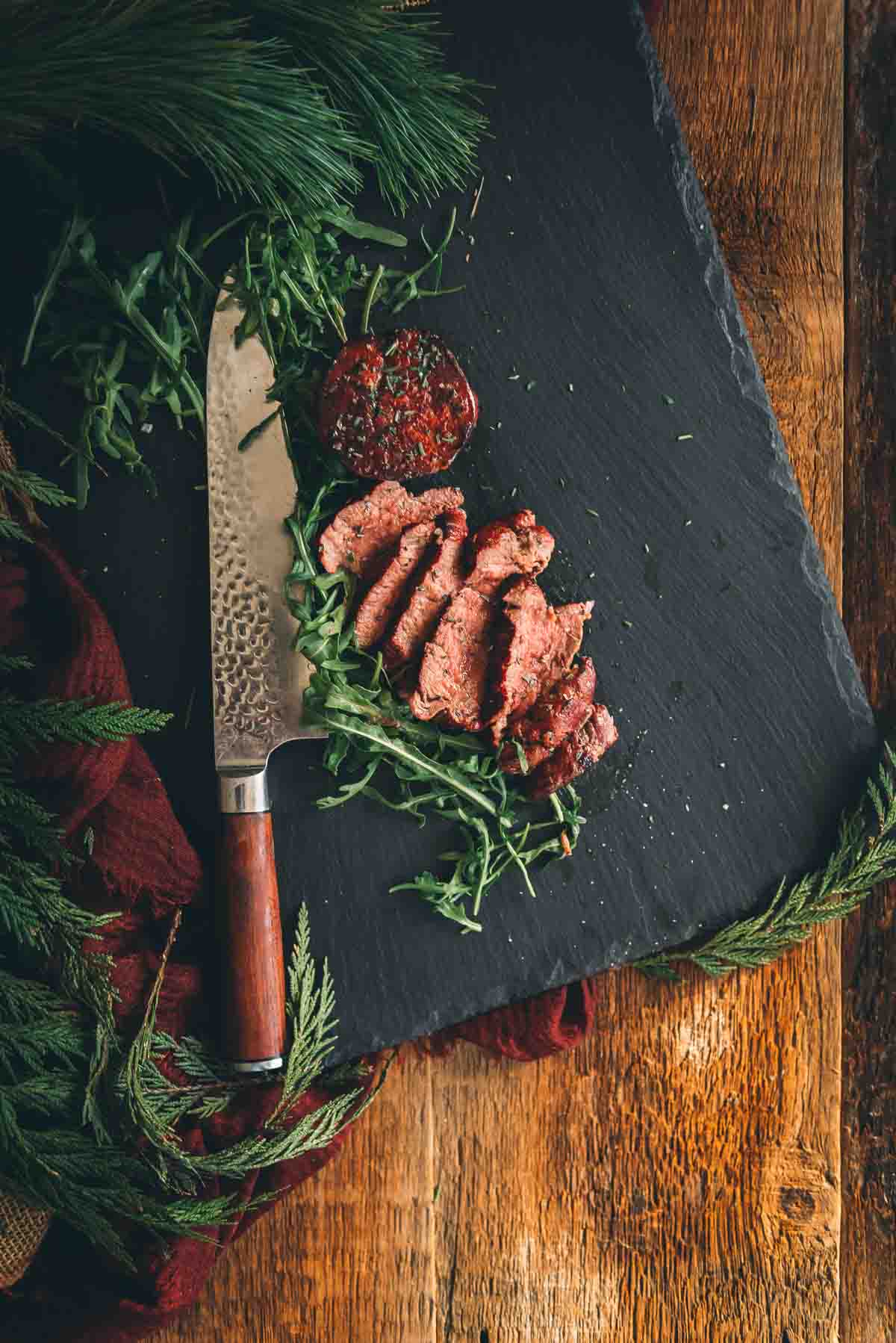 Grilled filet mignon steaks on a slate board, one sliced to show pink center and the other whole to show the crust.