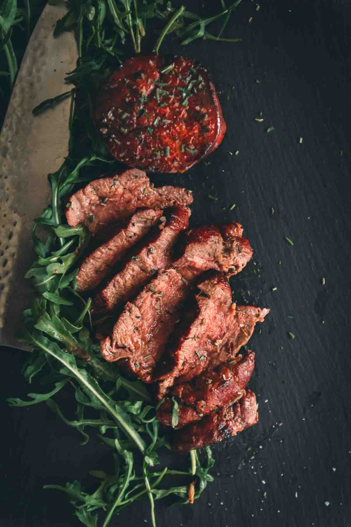 Steaks cooked perfectly with a medium rare rosy pink juicy center sliced on black slate. 