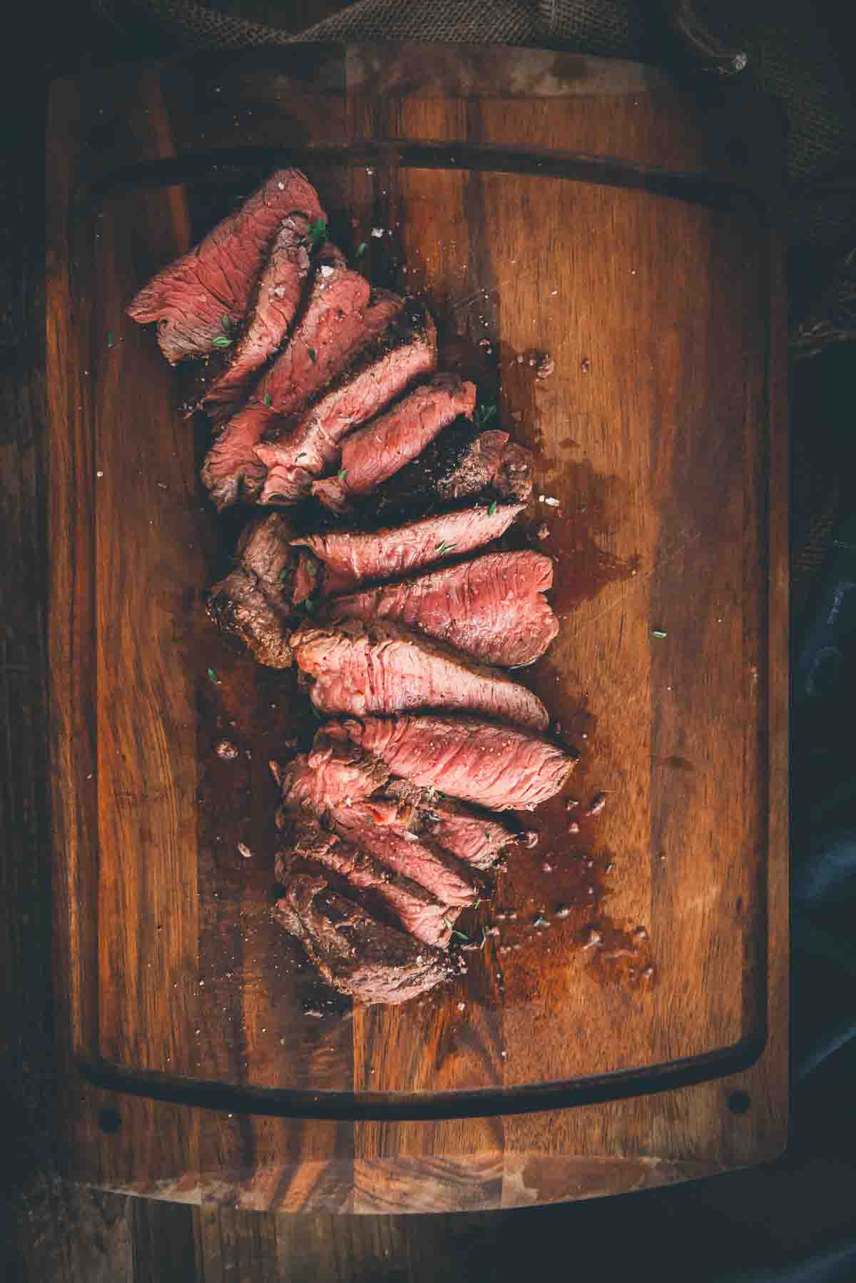 Overhead shot of steak, sliced to show medium rare center, fanned out on cutting board. 