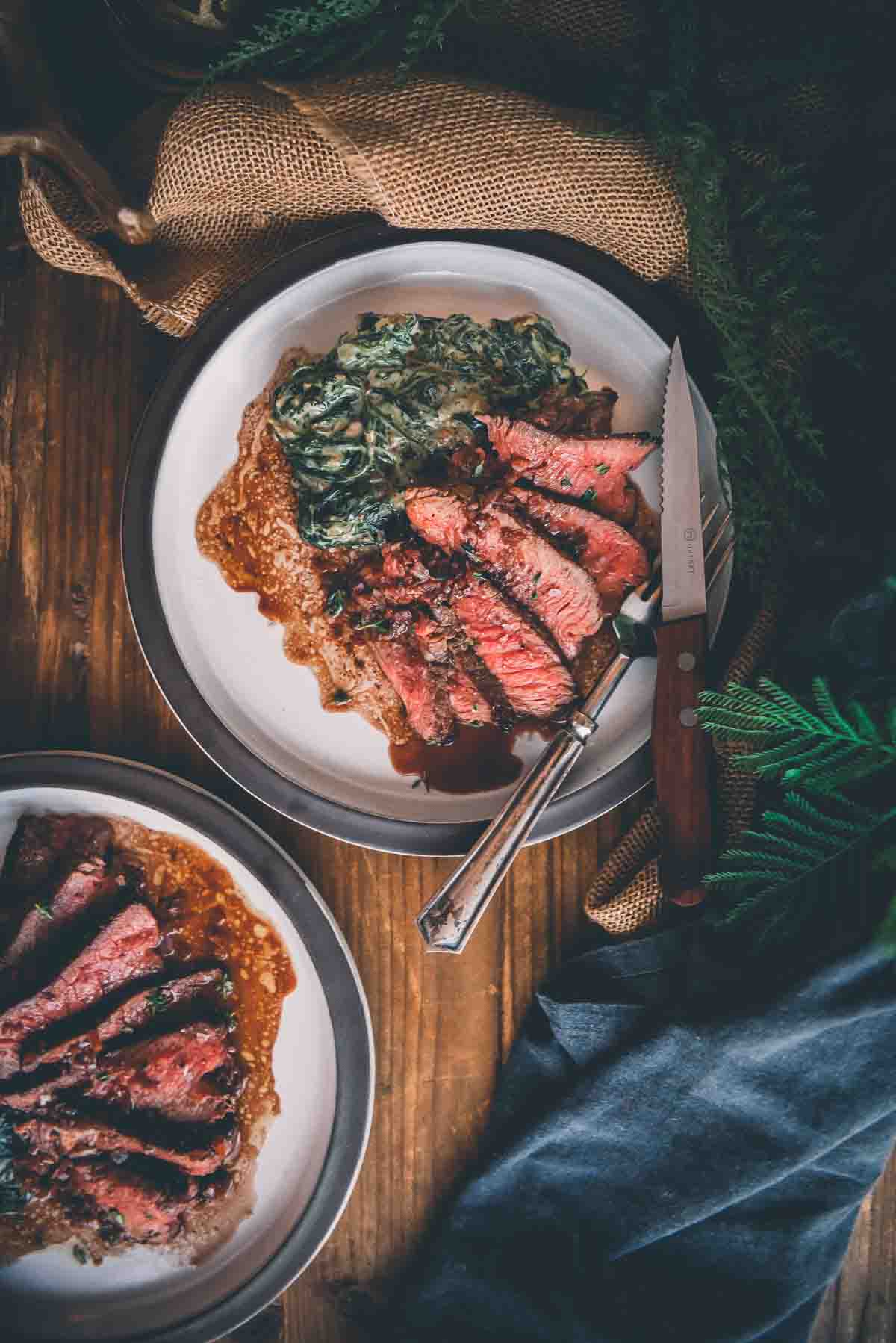 overhead shot of cooked sliced steaks on plates with red wine pan sauce and creamed spinach.