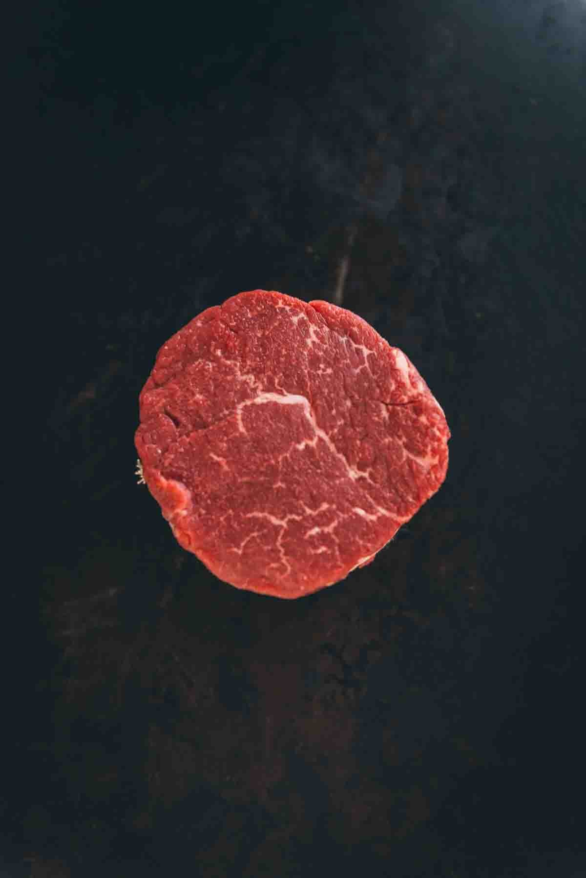 Raw tenderloin steak sliced to show lean white veins of marbling. 